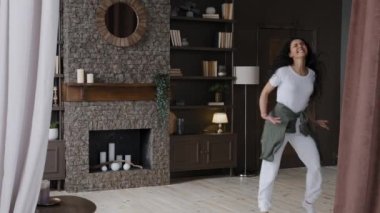 Happy joyful young woman dancing at home enjoying freedom weekend alone funny girl comedian having fun celebrating success making humorous dance movements active energetic dances to rhythmic music
