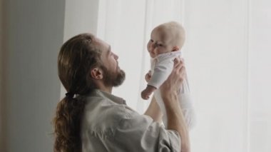 Caucasian bearded adult father throw up little cute smiling son daughter infant playing together at home tickling tummy of baby with nose dad holding newborn having fun with kid child tickle game