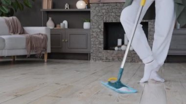 Close-up female legs graceful woman dancing rehearsing choreography while cleaning active energetic girl washes floor with mop in living room dances to music performs professional dance move at home