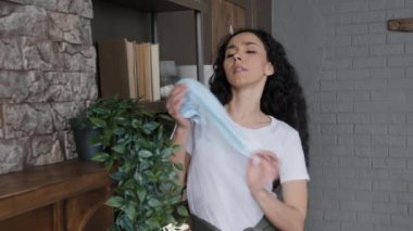 Expressive young curly hispanic woman wipes dust in room dancing to dynamic music energetic happy girl housewife enjoys household chores alone on weekend performs active dance move cleaning at home