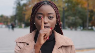 Close-up young confident mysterious african american woman standing outdoors showing silence gesture puts finger to mouth forbids speaking prohibits disclosure confidential information secret concept