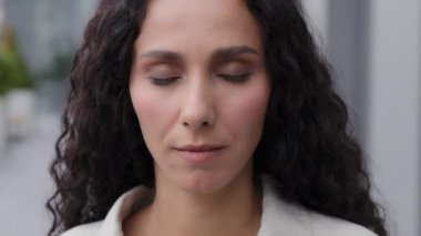Close up head shot portrait outdoors 30s beautiful calm serious sad upset woman look at camera outdoors. Gorgeous female girl with flawless face skin natural day make-up good eyesight blinking looking