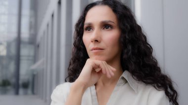 Close up pensive thoughtful puzzled Caucasian Hispanic thoughtfully girl woman with curly hair standing outdoors sad worry dreaming planning businesswoman thinking about idea solution problem thought