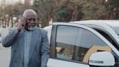 Cep telefonuyla konuşan yaşlı Afro-Amerikan bir adam arabaya doğru yürür ön koltukta oturur ve akıllı telefon kullanan yetişkin bir işadamı telefonla iş konuşmalarını tartışır.