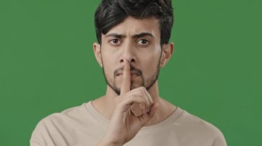 Close up serious arab guy looking at camera face young hispanic man hold index finger near mouth make silence shows gesture secret sign forbid speaking mystery gossip confidential information concept