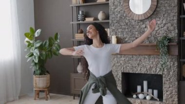 Happy young carefree woman housewife dancing in living room active attractive girl dancer performs ballroom dance at home shows choreographic movement beautiful cute hispanic female enjoying weekend