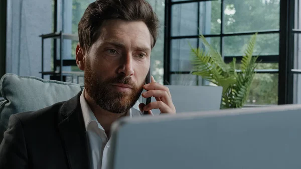 Angry bearded Caucasian adult 40s mad frustrated businessman arguing yelling conflict quarrel talking on phone looking at laptop computer sitting at office dissatisfied male client problem bad service