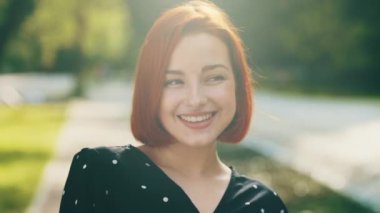 Smiling attractive redhead woman girlfriend caucasian millennial female model student lady girl smiling toothy smile feel calmness inhaling fresh air flirting posing in city park sun shine background