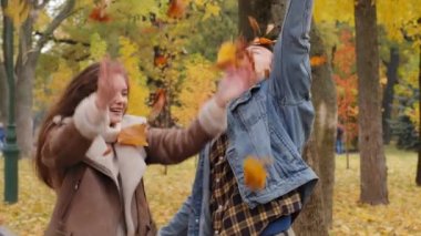 Positive caucasian young people youth couple partners man and woman spouses scatter leafage in autumnal park throw up autumn seasonal fallen leaves rejoice sunny day happy guy hug beloved girlfriend