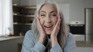 Delighted surprised mature middle-aged caucasian woman 60s lady looks amazed feel shock emotion win discounts triumph victory put hands on head. Elderly female retiree pensioner posing at home kitchen