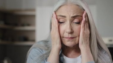 Sick old mature caucasian woman worried tired upset retiree grey-haired lady holding head massaging temples unbearable headache pressure suffering from migraine symptom panic attack feel pain at home