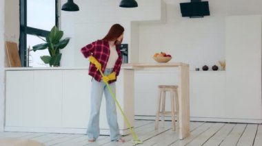 Young neat housewife redhead woman with long hair girl from cleanup agency take care of home house cleanliness washes floor with mop cleaning apartment modern kitchen room wipes wet scrubbing parquet