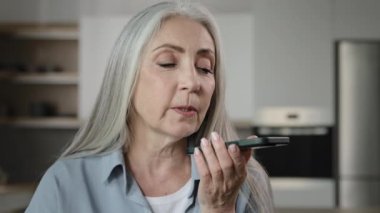 Elder lady caucasian gray-haired woman use modern technology records audio message at speakerphone send sound sms to family activate voice recognition at assistance mobile ai system no touching screen