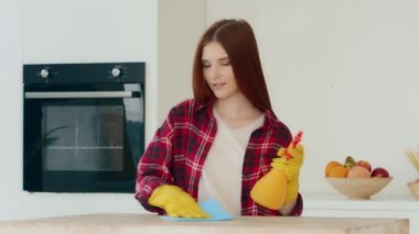 Redhead mistress housewife cleaner active young woman keeping house neat rhythmical wiping kitchen surface in rubber yellow gloves spraying liquid detergent on countertop cleaning with music dancing