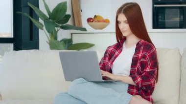 Caucasian 20s student work freelance on laptop at home female customer redhead businesswoman girl with long straight hair sits on sofa chatting online search job vacancy in internet play computer game
