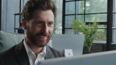 Close-up male worker leader Caucasian businessman bearded mature adult 40s manager looking at window smiling working with computer think about idea chatting online browsing programming job with smile