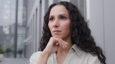 Close up pensive thoughtful puzzled Caucasian Hispanic thoughtfully girl woman with curly hair standing outdoors sad worry dreaming planning businesswoman thinking about idea solution problem thought