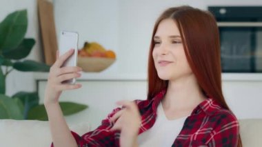 Attractive caucasian model girl taking selfie photo redhead young woman blogger recording video blog on telephone waving hello at mobile camera streaming video chat meeting online with friend indoors