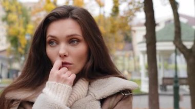 Doubtful pensive young woman brunette caucasian girl stand alone in autumn urban park holds hand to chin looking around waiting for boyfriend late feels lonely worries think difficult decision unsure