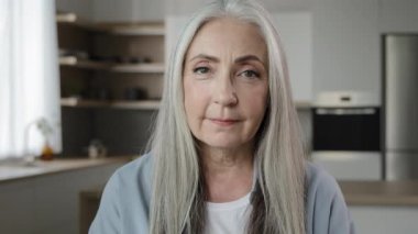 Portrait calm confident adult middle-aged woman pensioner granny mistress homeowner tender mature old lady with long grey hair posing in kitchen room serene looking at camera healthy beauty appearance