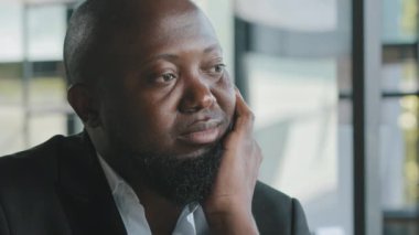 Bored unhappy sad african male american lazy adult guy dreaming about end working day expressing passive facial emotion feel boredom lack of motivation sit in office depression problem mental health