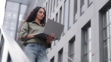 Successful 30s businesswoman working typing on laptop using free city Wi-Fi chatting on wireless computer standing near office company building female CEO boss leader woman analyze financial project
