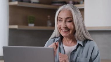 Caucasian mature middle-aged female pensioner woman chatting online distance communication remote with family children during quarantine looking at laptop screen surprised glad to see virtual friends