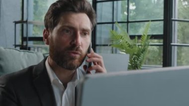 Angry bearded Caucasian adult 40s mad frustrated businessman arguing yelling conflict quarrel talking on phone looking at laptop computer sitting at office dissatisfied male client problem bad service