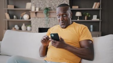 Middle-aged 50s senior african winner american grandfather buyer player make online bet on phone gadget successful internet deal play mobile game win lottery receive good sms rejoice triumph victory