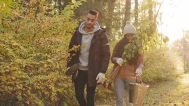 Young couple of happy people walking in autumn park talk eco activists guy and girl going to plant tree volunteers care about environment discuss planting plants organization for conservation nature