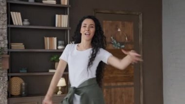 Young happy energetic hispanic woman dancing merrily to favorite music at home alone pretty female dancer choreographer rehearsing dance in room enjoying playful domestic activity celebrating freedom