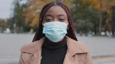 Close-up young serious stylish african american woman standing outdoor wearing medical protective mask recovered girl takes off respirator posing looking at camera concept prevention during quarantine