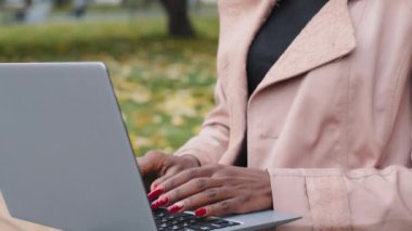 Young african american woman freelancer typing on laptop working outdoors focused girl journalist writes article writing note using computer application female student studying remotely in autumn park