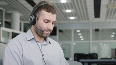 Young businessman sitting in office talking to employees at online conference communicating with client by headset with microphone helpline worker speaks to customer remotely uses modern technology