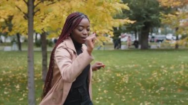 Carefree happy young african american woman dancing energetic in autumn park joyful girl active moving to music outdoors celebrating success enjoying walk performing dance move feeling pleasure joy