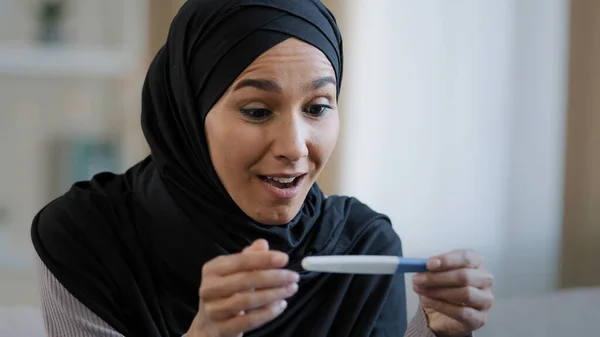 Joyful islamic young woman in hijab smiling happily holding pregnancy test excited pregnant lady surprised and happy celebrating good news future mother shows positive result muslim female expect baby
