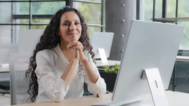 Young pretty cute hispanic businesswoman sitting in office looking at camera happy confident girl entrepreneur model posing at workplace smiling presenting advertising successful business corporation