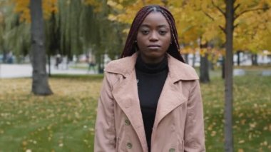 Serious young african american woman standing in park posing outdoors looking at camera shaking head negative response deflection reaction disagree sign prohibition rejection ban disagrees answers no