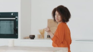 African American cheerful woman housewife with curly hair in kitchen enjoy music with laptop dancing having fun spin whirling dance listening audio in morning before breakfast funny move active moving