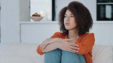 Alone pensive thoughtful puzzled confused stressed sad unhappy African woman sitting on sofa at home thinking about problem trouble feeling bad frustrated abdominal painful discomfort menstruation