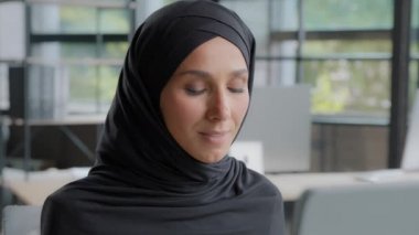 Close-up young attractive arab businesswoman sitting in office working on computer successful female professional worker developer developing startup strategy looking at camera posing at workplace