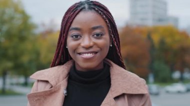 Female portrait close-up young satisfied happy african american woman standing in autumn park looking at camera smiling with white teeth attractive joyful girl model with stylish hair posing outdoors