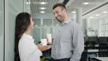 Diverse colleagues communicate during lunch break in office drinking coffee from paper cups enjoy pleasant conversation discuss project share ideas employees talking concept of friendship at work