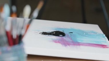 Close-up black dark paint splatters on canvas with pink and blue color picture female hand holding paint brush draws making texture creates masterpiece work of art painting preparing for exhibition