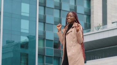 Happy young african woman having fun funny dancing against office building background carefree happy joyful girl businesswoman student actively dances outdoors celebrating victory rejoices in success