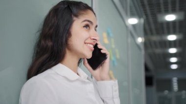 Young positive woman office worker manager talking to client on mobile phone remote consultation using smartphone friendly girl makes online order speaks on telephone advises client advertises product