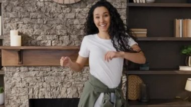 Happy excited young woman celebrating victory enjoying success excited energetic girl winner dances victory dance rejoices funny moving falls on sofa in room having fun at home on weekend laughing