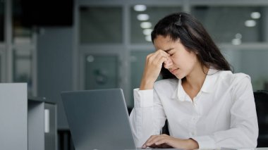 Young stressed tired overworked female office worker working on laptop suffering from eye fatigue massages bridge of nose feels tense headache from overwork having painful feeling exhausted tiredness