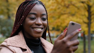 Close-up young happy woman standing in autumn park communicates video chat on smartphone friendly online conversation joyful smiling girl talking with friend on webcam on phone answering video call