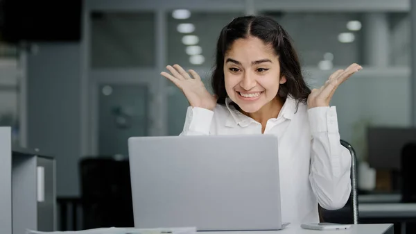 Young woman manager sitting in office looking at laptop screen receiving notification reads good news rejoices in success celebrating victory feels good luck receives promotion at work gets job bonus